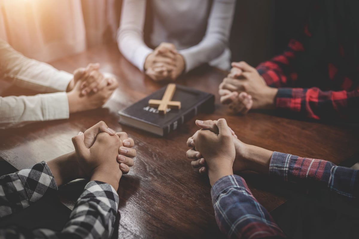 Group of Christian holding hands praying worship together to believe and Bible on a wooden table for devotional for prayer meeting concept, teamwork.